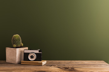 Vintage camera and cactus on a wooden desk with green wall.