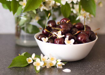 Ripe juicy cherry in a white bowl on a background of flowers. Summer berries. Healthy food.