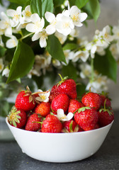 Ripe juicy strawberries in a white bowl on a background of flowers. Summer berries. Healthy food.