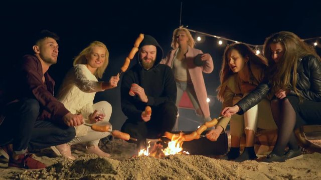 friends hang out on campsite young people cook sausages on Fire and dance while enjoy holiday outdoors in lighting lamps