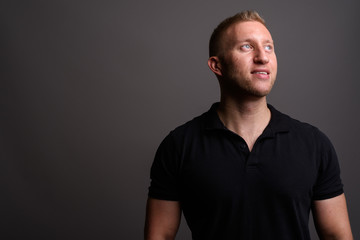 Fototapeta premium Man with blond hair wearing black polo shirt against gray backgr