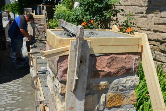 Mauersetzer rekonstruieren eine Gartenmauer aus buntem Natur-Sandstein fachmännisch: Glattstrich des Mauerabschlusses in der  Schalung, Hessen, Deutschland