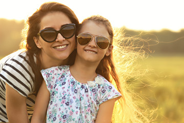 Happy fashion kid girl embracing her mother in trendy sunglasses and looking on nature background. Closeup portrait of happiness.