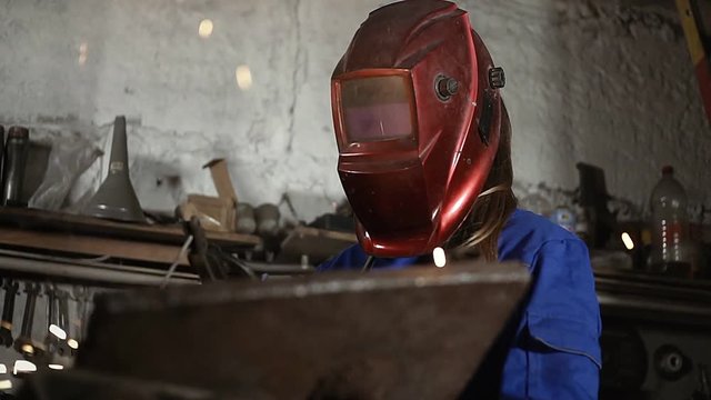 cute welder girl in uniform in the garage working with welding equipment. Women's work in art