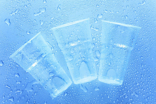 Three disposable plastic cup with water drops on a blue background