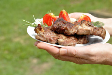 Grilled meat cooked on a grill in a white plate with slices of a tomato.