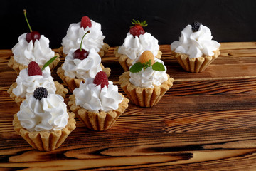 Nine cakes with protein cream and summer berries on wooden table. Black background, selective focus. Place for text