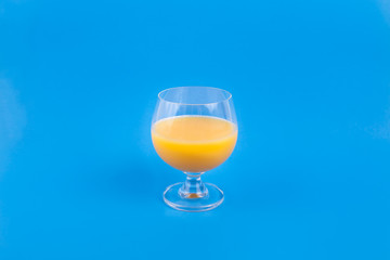 Fancy clear glass of orange juice on a solid blue background 