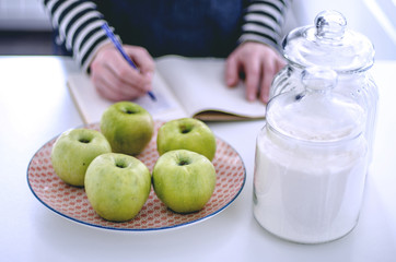 Green apples on a plate to make a pie and the girl writes a recipe on the background