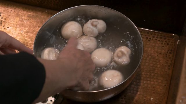 Hands cleaning white mushrooms in water in a bowl