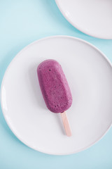 One raw vegan blueberry popsicle on white plate from above. Pastel blue background. Minimalism food photography, blogging concept. Geometric style.  Copyspace
