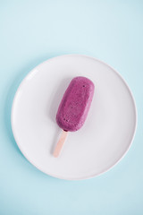 One raw vegan blueberry popsicle on white plate from above. Pastel blue background. Minimalism food photography, blogging concept. Geometric style.  Copyspace