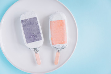Ice-cream, popsicles wrapped in silver aluminium foil from above on a round plate. Pastel blue...