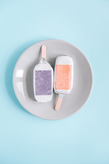 Ice-cream, popsicles wrapped in silver aluminium foil from above on a round plate. Pastel blue...