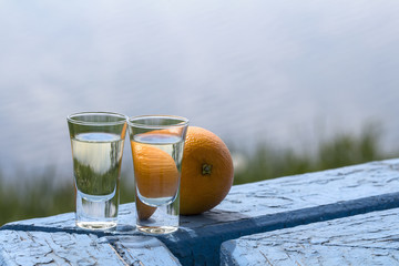 Two shots of tequila with orange are on the table by the beach