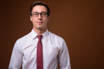 Young handsome businessman wearing eyeglasses against brown back