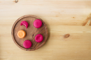 Berry crimson pink macaroons from raspberry and orange Parisian French macaroon from mango on a wooden authentic plate on a wooden texture table.