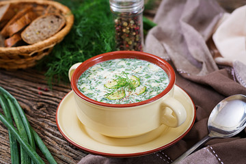 Summer yogurt cold soup with egg, cucumber, and dill on wooden table. Okroshka. Russian food