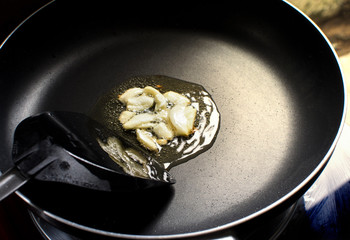 Garlic fry on a vegetable oil in a black hot pan and plastic spade at kitchen in home.