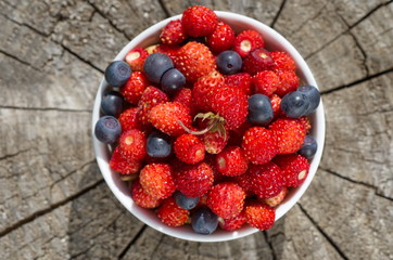 Bowl with strawberries and blueberries on a wooden background close-up © koromelena