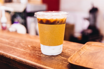 Iced latte in paper wrap plastic cup on wooden counter.