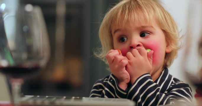 Cute adorable Candid real life toddler child looking at screen while chewing food. Child with red cheaks hypnotized by screen