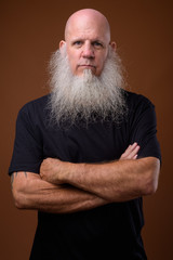 Mature bald man with long gray beard against brown background