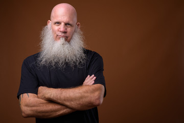 Mature bald man with long gray beard against brown background