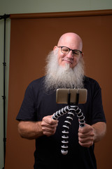Mature bald man with long gray beard against brown background