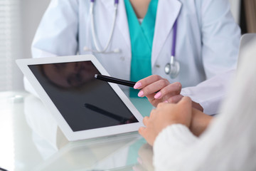 Doctor and patient, close-up.  Physician pointing into touch pad screen of tablet computer....