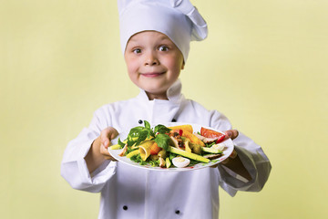 funny boy chef cooked salad with vegetables, cheese and ham on a plate