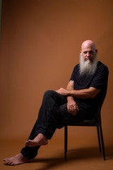 Mature bald man with long gray beard against brown background