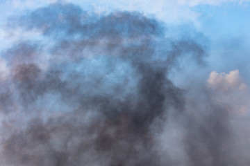 Black smoke against a blue sky with clouds