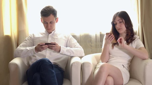Young man and woman with telephones in armchairs.