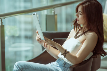 Young Asian lovely creative and businesswoman holding tablet in relaxing time and working on tablet computer at the new modern style office glasses building, new technology equipment concept.