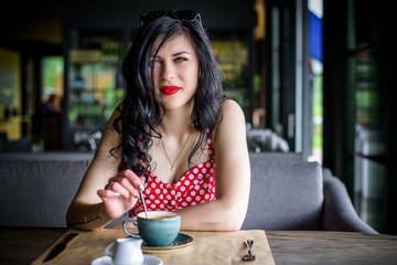 Fashion retro style portrait of young beautiful woman in polka dot dress.   Retro (vintage) portrait of the alluring young girl sitting in cafe. Pin up style portrait of young girl in dress 