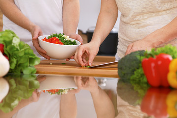 Closeup of human hands cooking in kitchen. Mother and daughter or two female friends cutting vegetables for fresh salad. Healthy meal, vegetarian food and lifestyle concepts