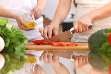 Fotobehang Closeup of human hands cooking in kitchen. Mother and daughter or two female friends cutting vegetables for fresh salad. Healthy meal, vegetarian food and lifestyle concepts © rogerphoto
