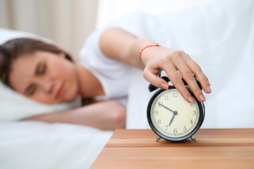 Sleepy young woman stretching hand to ringing alarm willing turn it off. Early wake up, not getting enough sleep concept