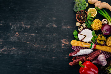 Assortment of sausage, cheese and fresh vegetables. Italian cuisine. On a black wooden background. Top view. Copy space.