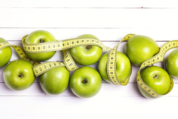 Green apples and yellow centimeter tape on white wooden background with space for text, top view.