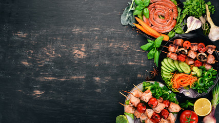 Assortment of baked barbecue meat. Sausages, skewers, fresh vegetables. Tomatoes, onions, garlic. On a wooden background. Copy space.