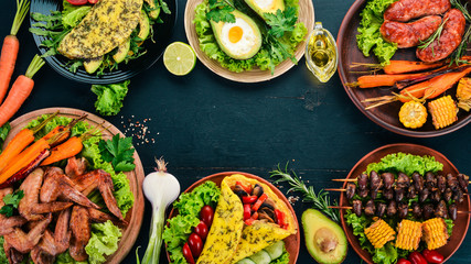 Food. Avocado dishes, chicken wings, omelet and barbecue. On a wooden background. Top view. Copy...