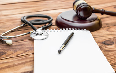 Blank notepad with gavel and stethoscope on wooden table.