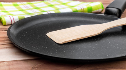Empty pan with wooden spade and kitchen towel on wooden table.