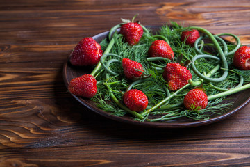 Strawberries and greens on a brown plate on wooden background. Copy space