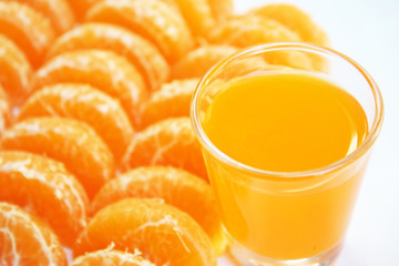 Glass of orange juice and pieces of mandarin orange on white plate background