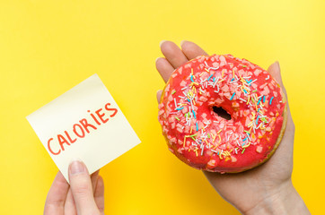 Female hand holding pink donut with sprinkles extra calories fat fast food excess weight unhealthy...