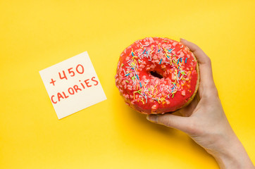 Female hand holding pink donut with sprinkles extra calories fat fast food excess weight unhealthy...