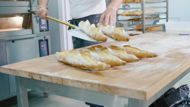 Professional baker taking bread out from the oven in a commercial kitchen
